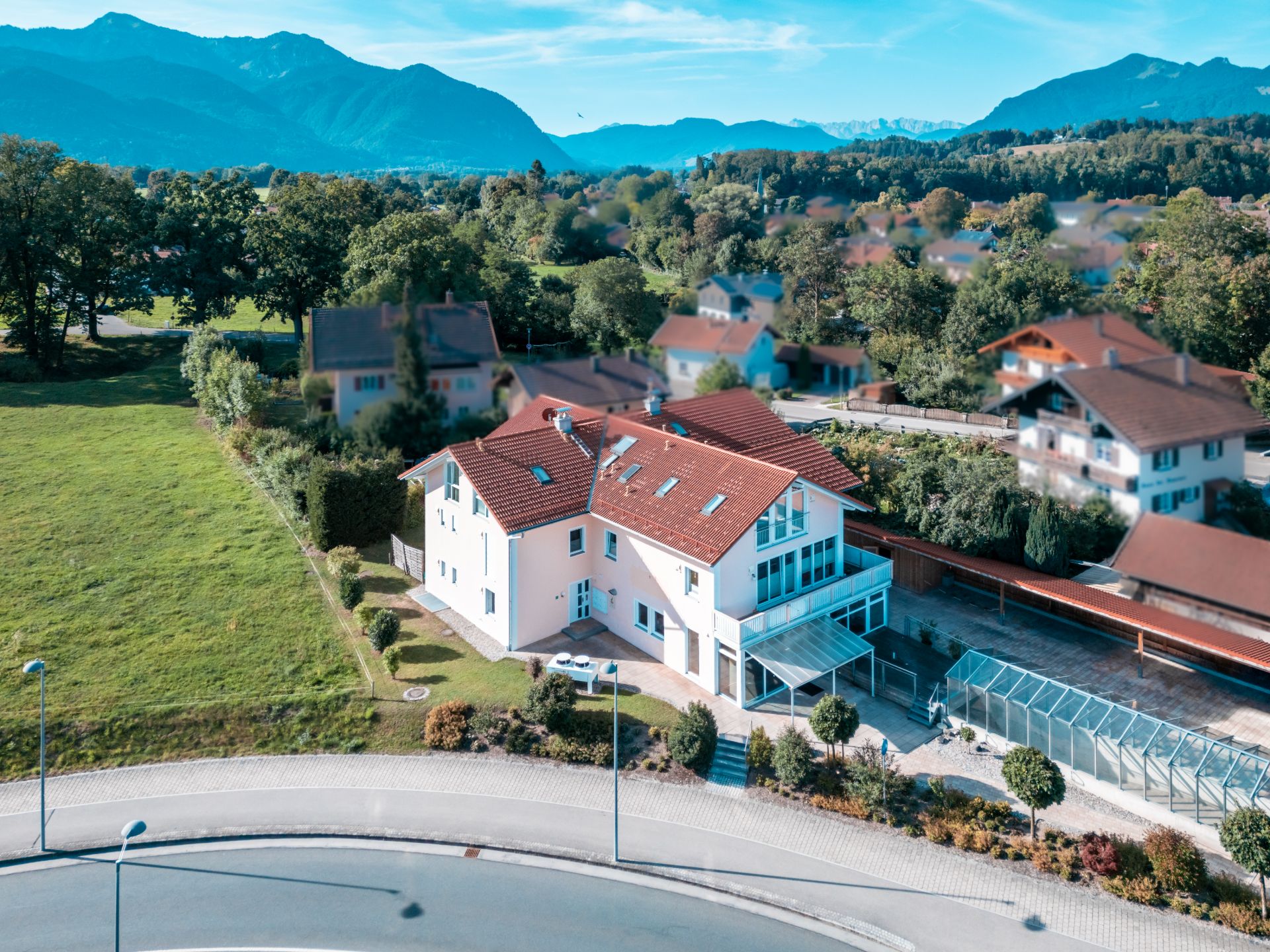 Luftaufnahme eines Wohnhauses mit rotem Dach neben einer Straße und viel Grün.