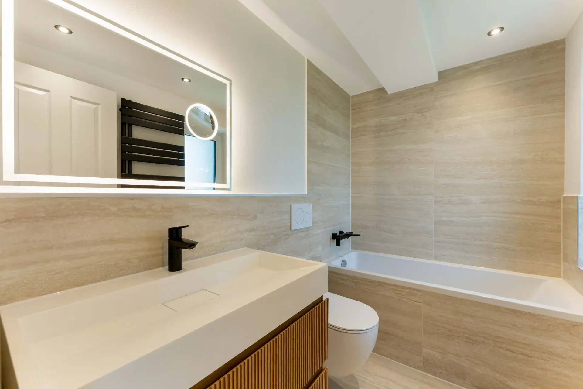 Modernes Badezimmer mit Badewanne, großem Spiegel und Waschbecken.
