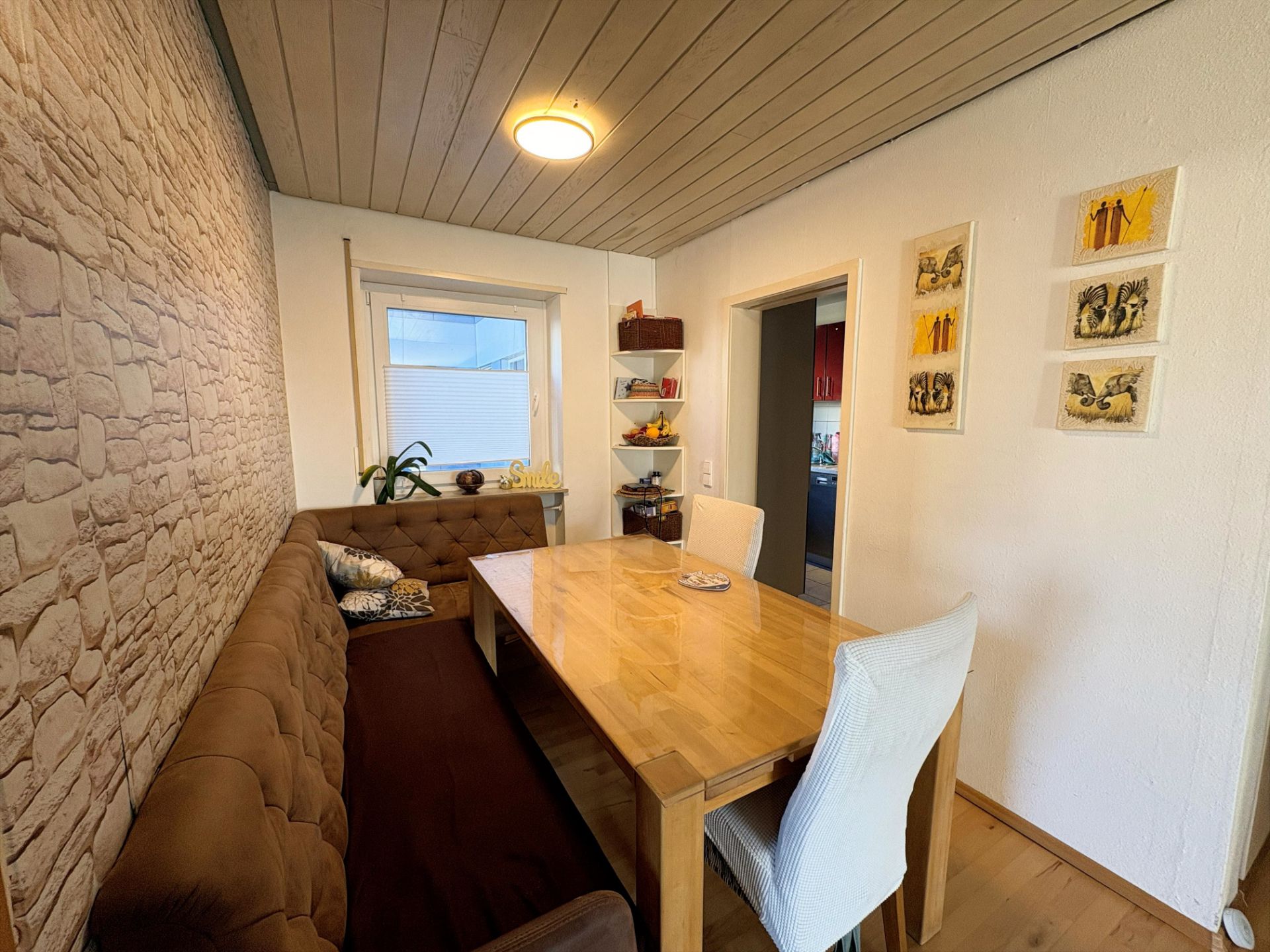 Esszimmer mit Holztisch, brauner Eckbank, zwei weißen Stühlen und Bildern an der Wand.