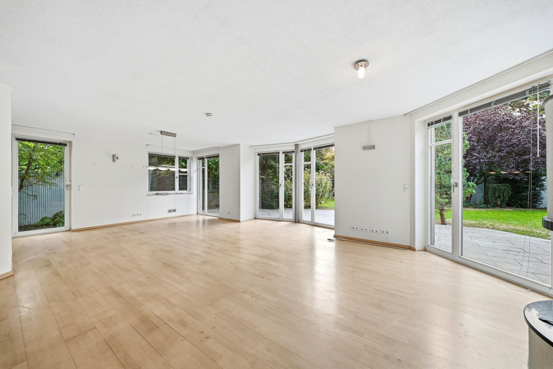 Heller, leerer Wohnraum mit großen Fenstern und Blick auf einen Garten.