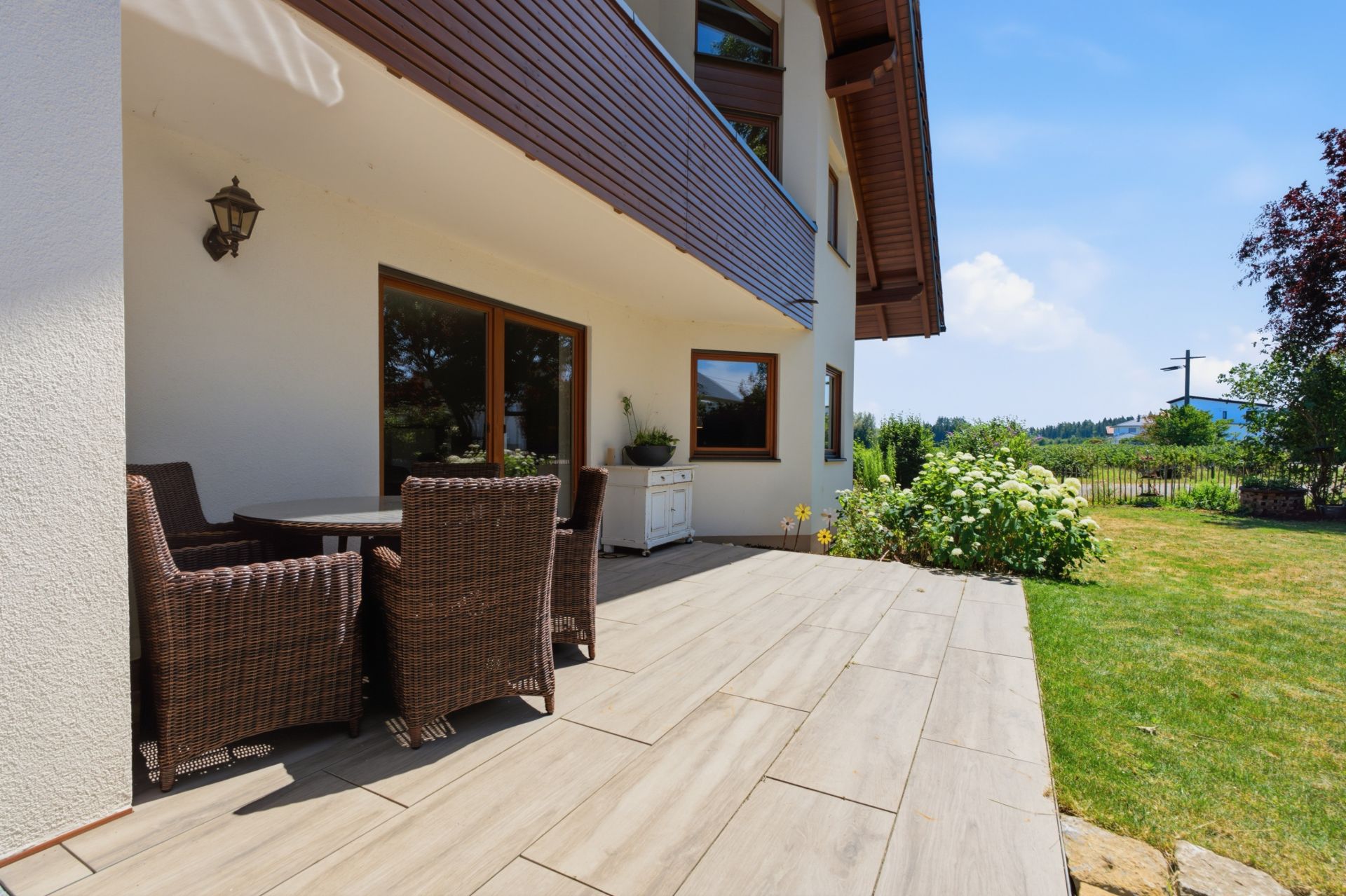 Moderne Terrasse mit Rattanmöbeln und Blick auf einen Garten neben einem Wohnhaus.