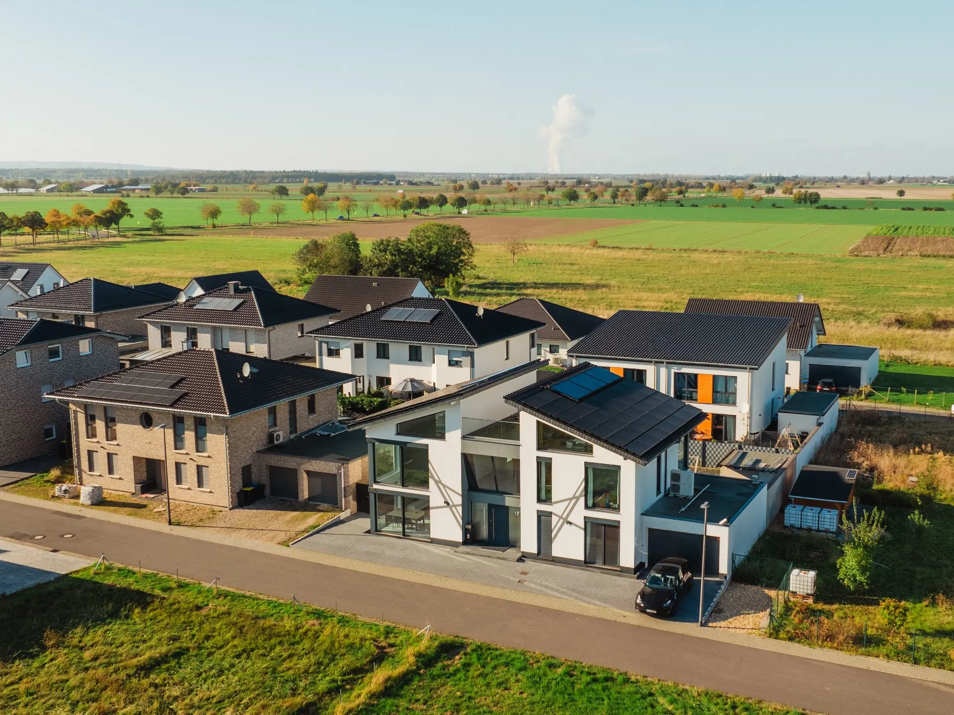 Luftaufnahme von modernen Einfamilienhäusern mit Solaranlagen in einem Wohngebiet am Feldrand.