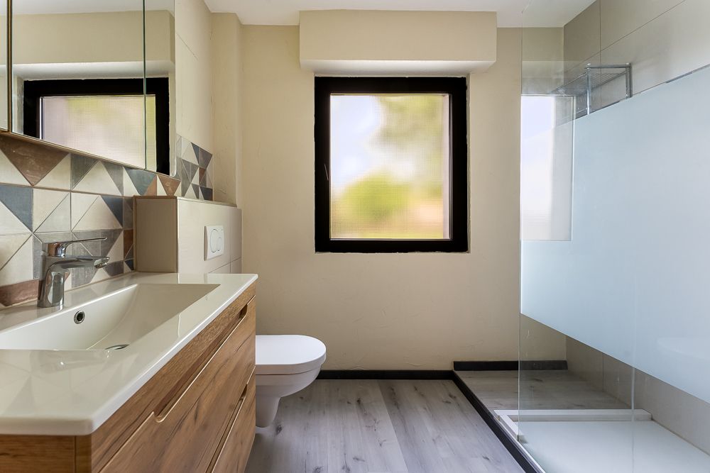 Modernes Badezimmer mit Holzmöbeln, Waschbecken, Toilette, Fenster und Dusche.