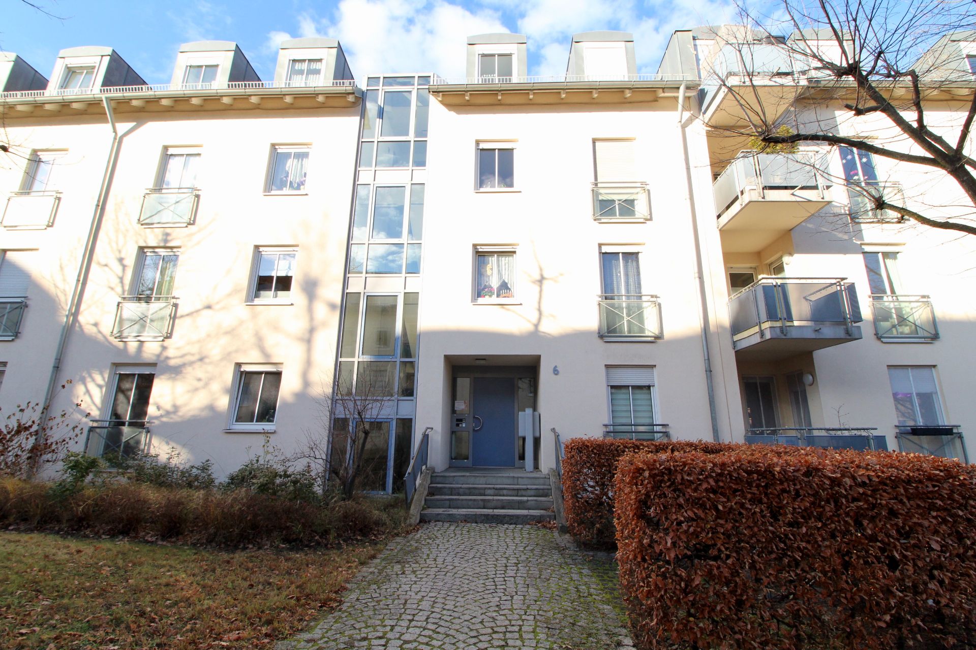 Eingang eines modernen Mehrfamilienhauses mit Balkonen und Glasfassade.