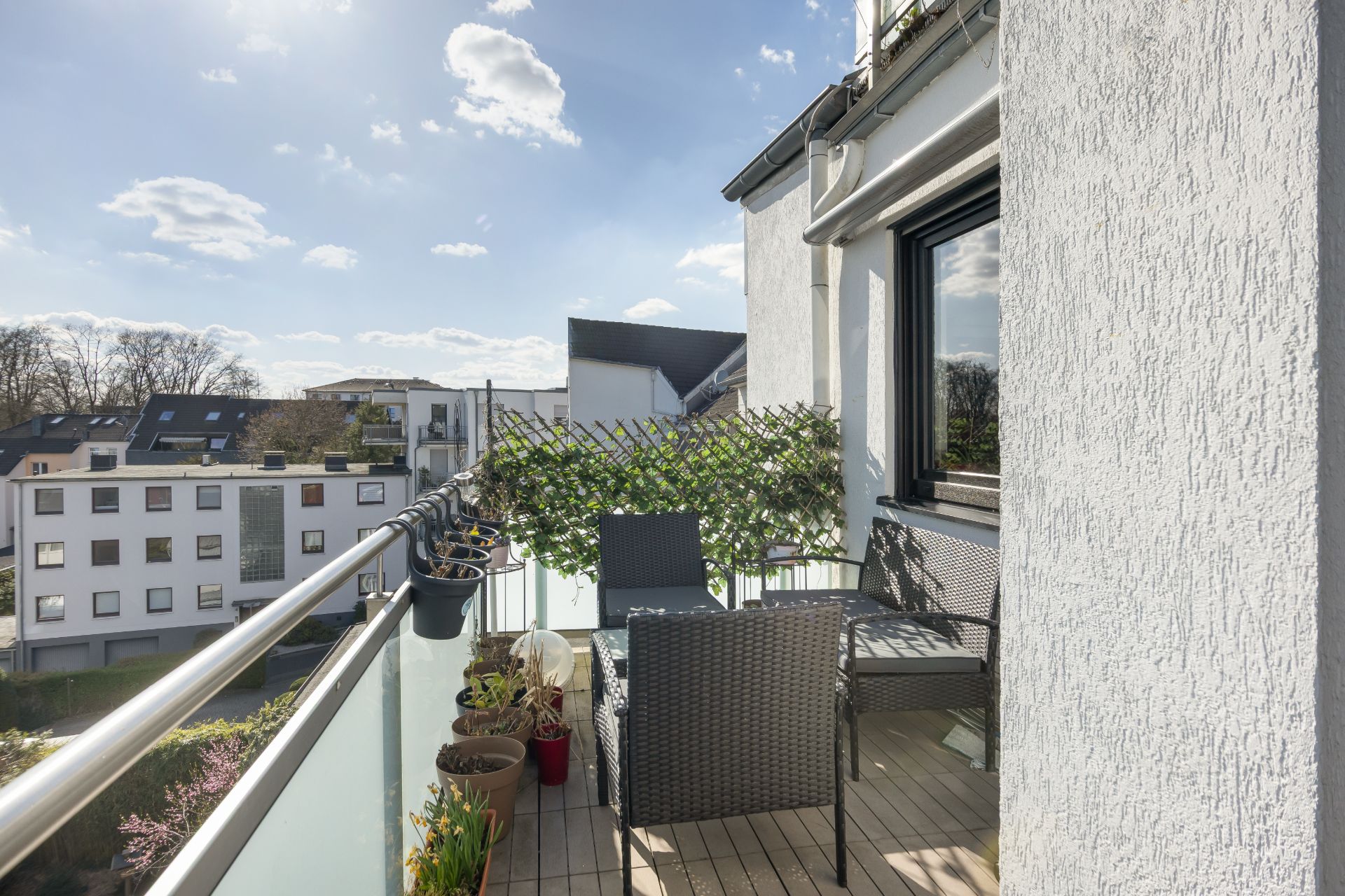 Balkon mit zwei Stühlen, Tisch, Pflanzen und Blick auf Wohngebäude bei Tageslicht.