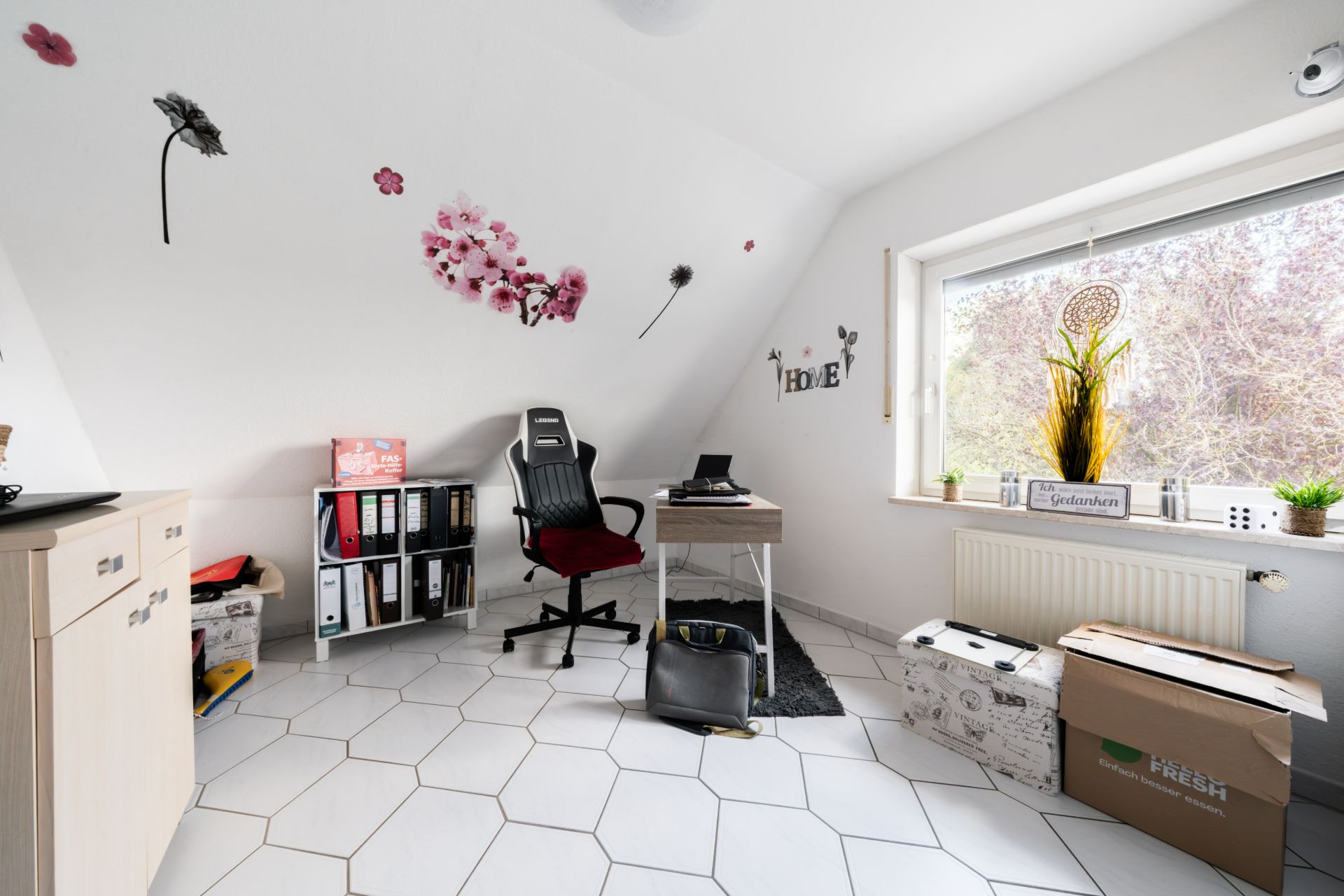 Helles Arbeitszimmer mit Schreibtisch, Stuhl, Regal, Kartons und bunten Wandstickern.