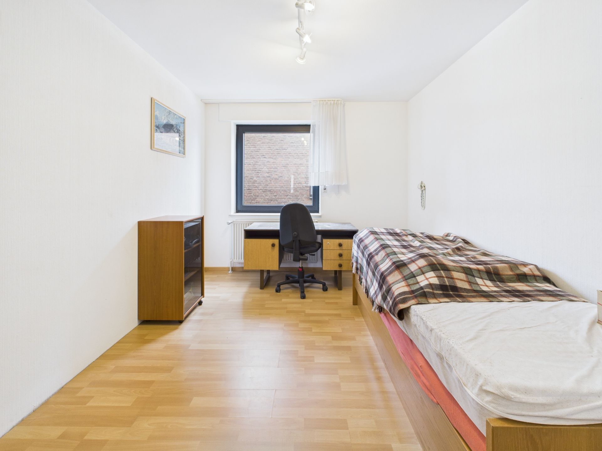 Helles Zimmer mit Einzelbett, Schreibtisch, Stuhl, Kommode und Fenster.