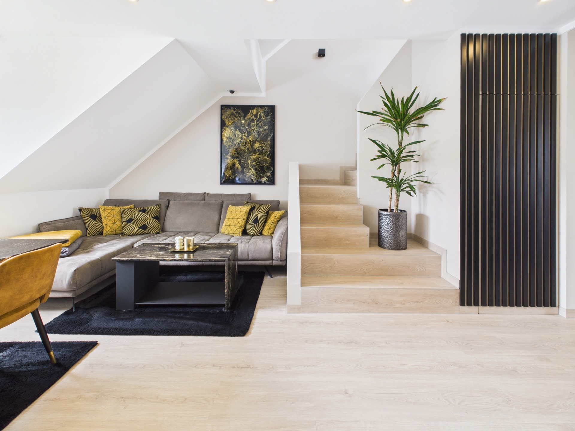 Modernes Wohnzimmer mit grauem Sofa, Couchtisch, Pflanze und Treppe.