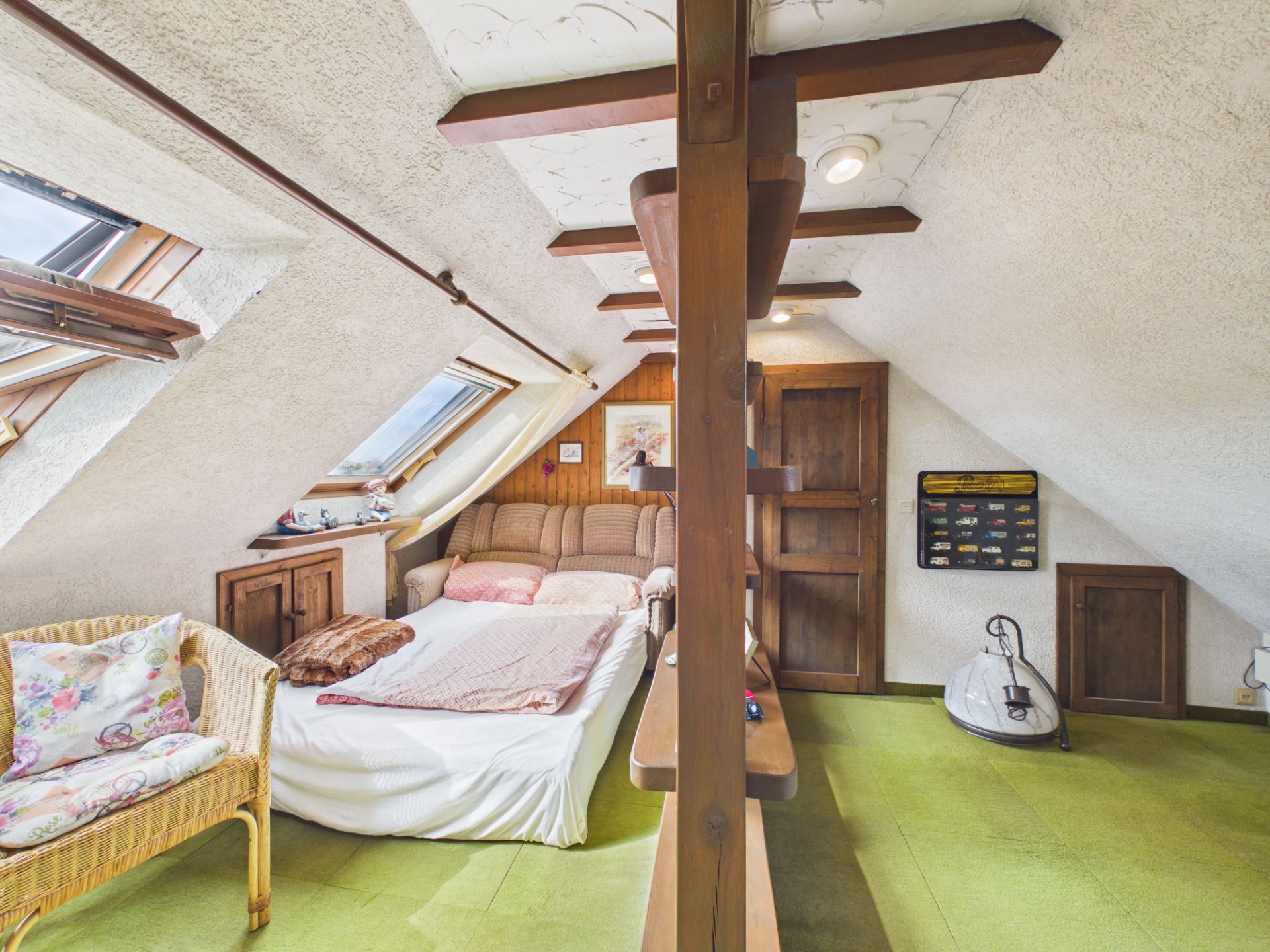 Gemütliches Dachzimmer mit Bett, Korbstuhl, Holzregal und Dachfenstern.