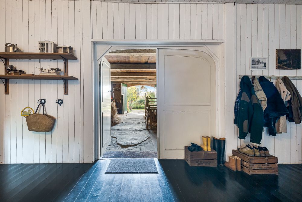 Eingangsbereich mit Holzwand, Regalen, Jacken, Schuhen und offenem Blick nach draußen.