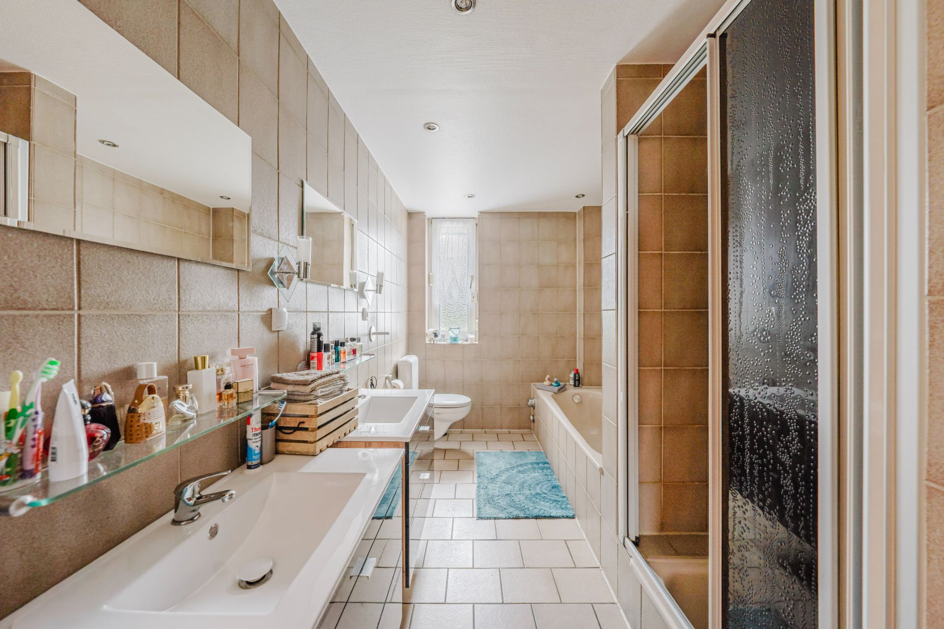 Helles Badezimmer mit Doppelwaschbecken, Badewanne, Dusche und großem Fenster.