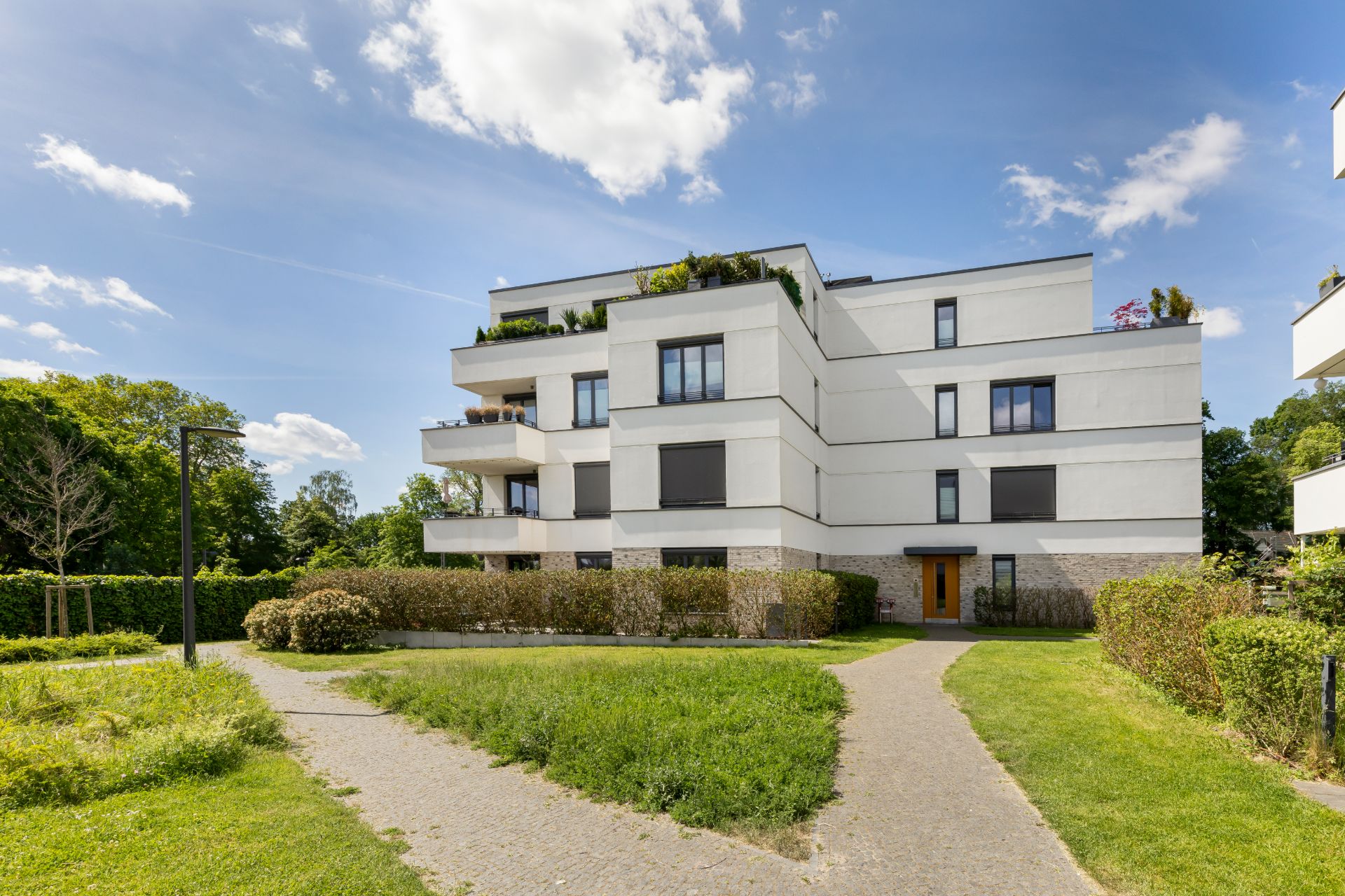 Modernes, weißes Wohngebäude mit Balkonen, umgeben von Grünflächen und Gehwegen.