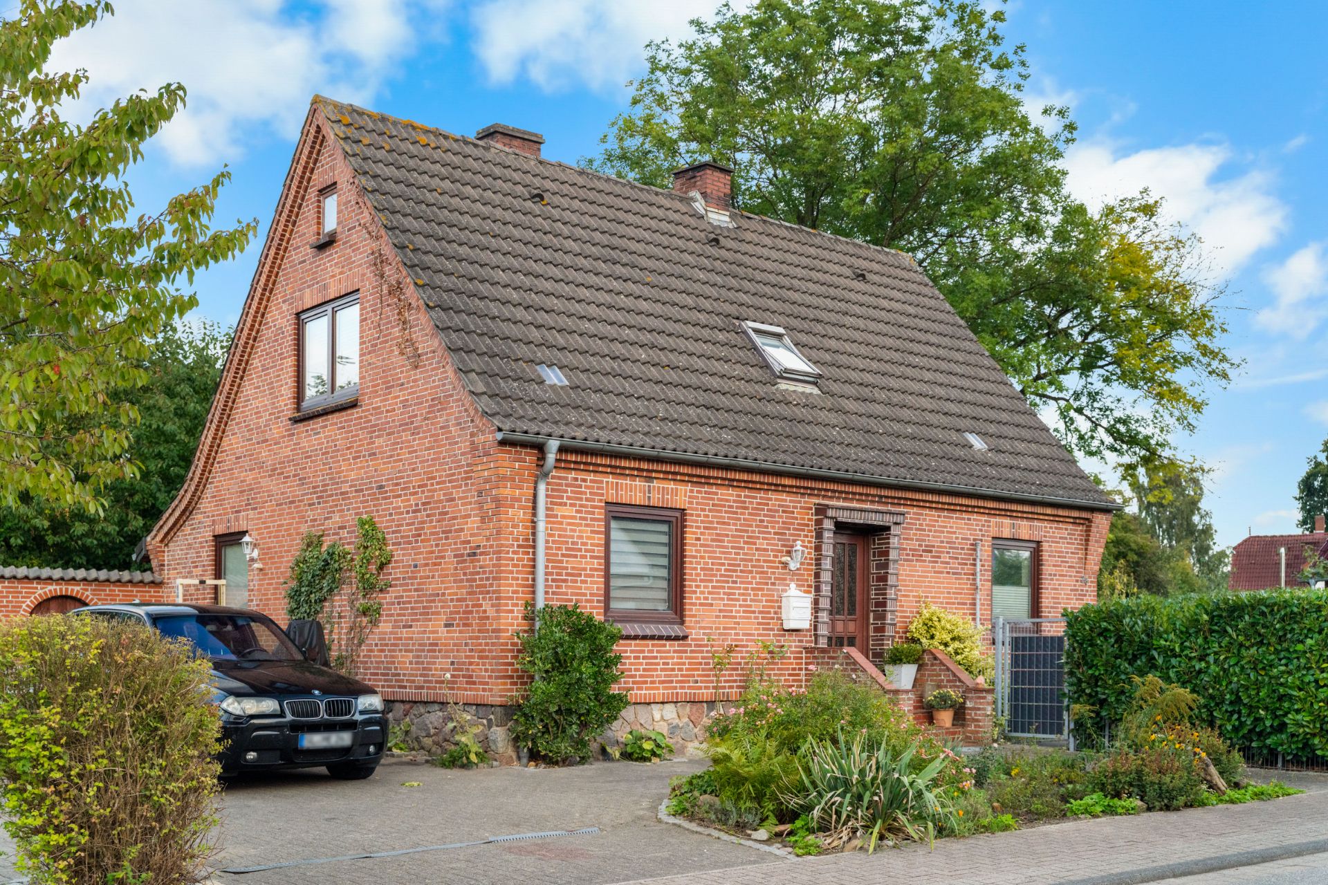 Backsteinhaus mit Satteldach, Vorgarten und geparktem Auto in Einfahrt.
