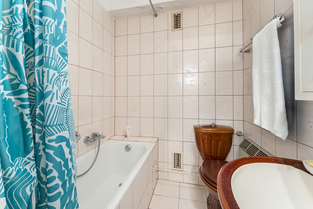 Badezimmer mit Badewanne, brauner Toilette, Waschbecken und blauem Duschvorhang.