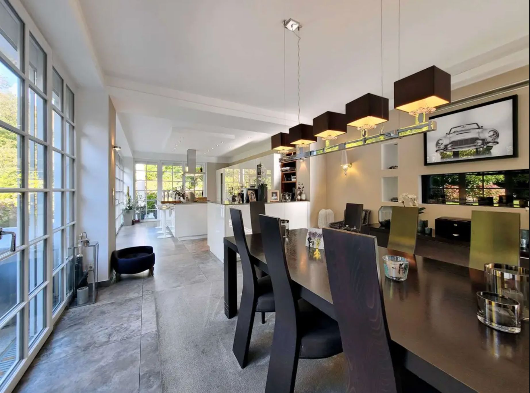 Modernes Esszimmer mit großem Tisch, schwarzen Stühlen und großen Fenstern, Blick auf offene Küche.