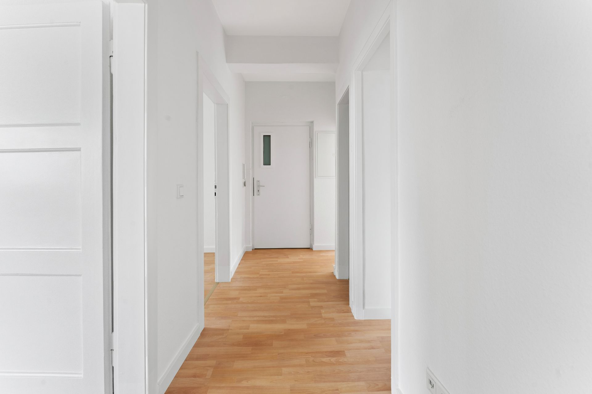 Heller Flur mit weiß gestrichenen Wänden und Holzboden, mehrere Türen führen zu anderen Räumen.