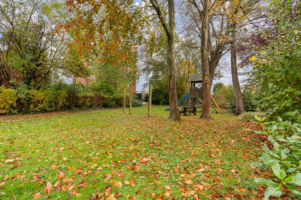 Grüner Garten mit Herbstlaub, Bäumen und einem Holz-Klettergerüst mit Rutsche.