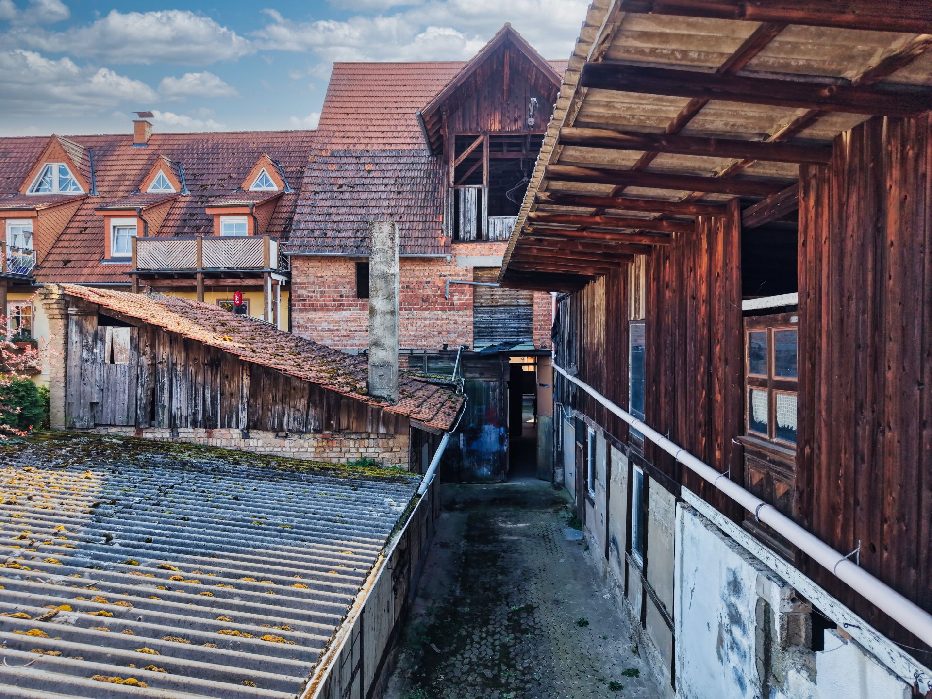 Mehrere alte Holz- und Ziegelgebäude um einen schmalen, gepflasterten Innenhof.