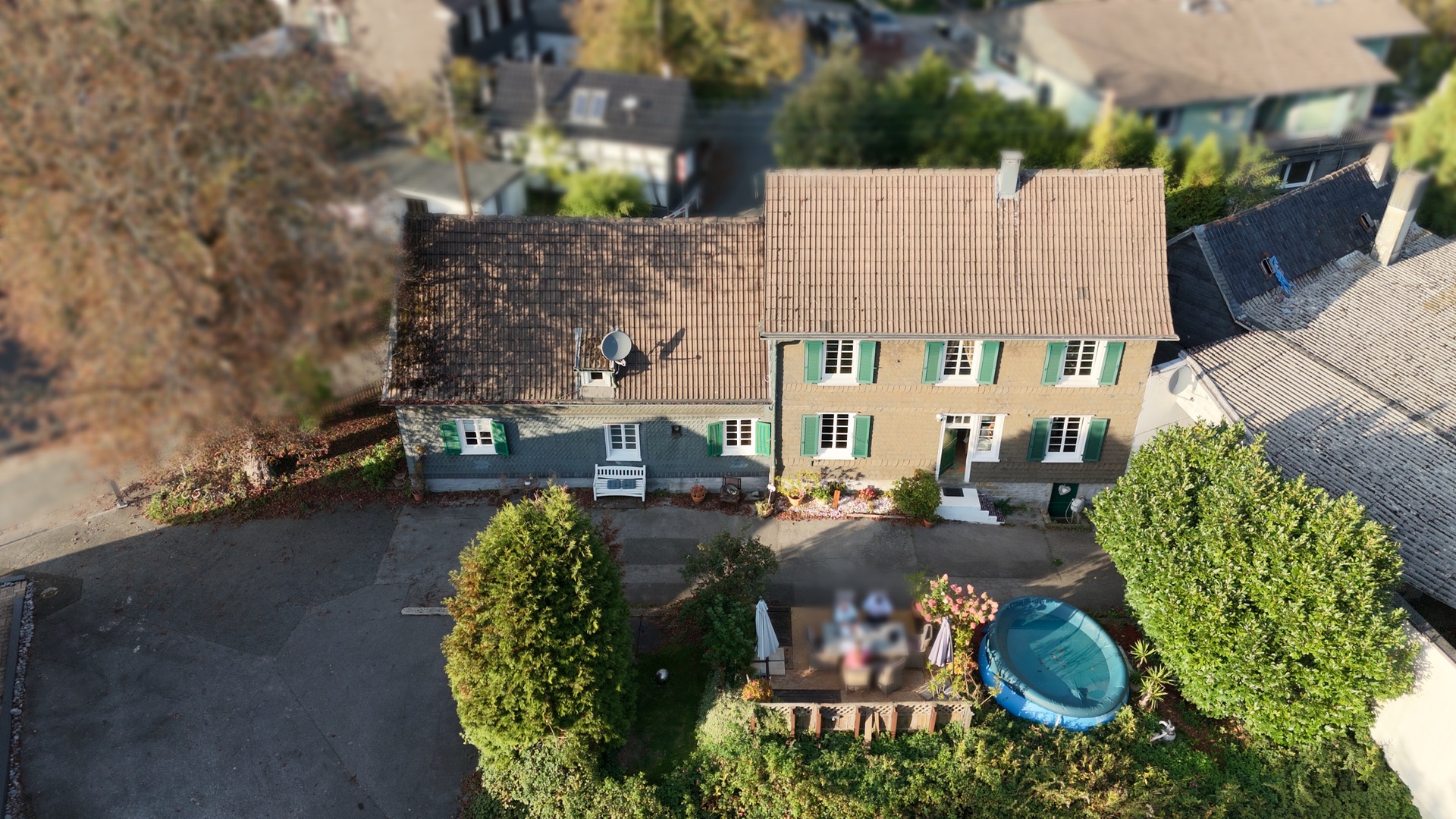 Luftaufnahme eines grünen Wohnhauses mit Terrasse, Garten und kleinem aufblasbaren Pool.