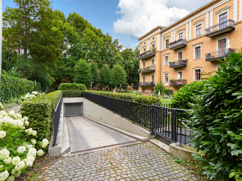 Auffahrt zur Tiefgarage vor einem Wohngebäude mit Balkonen und viel Grün.