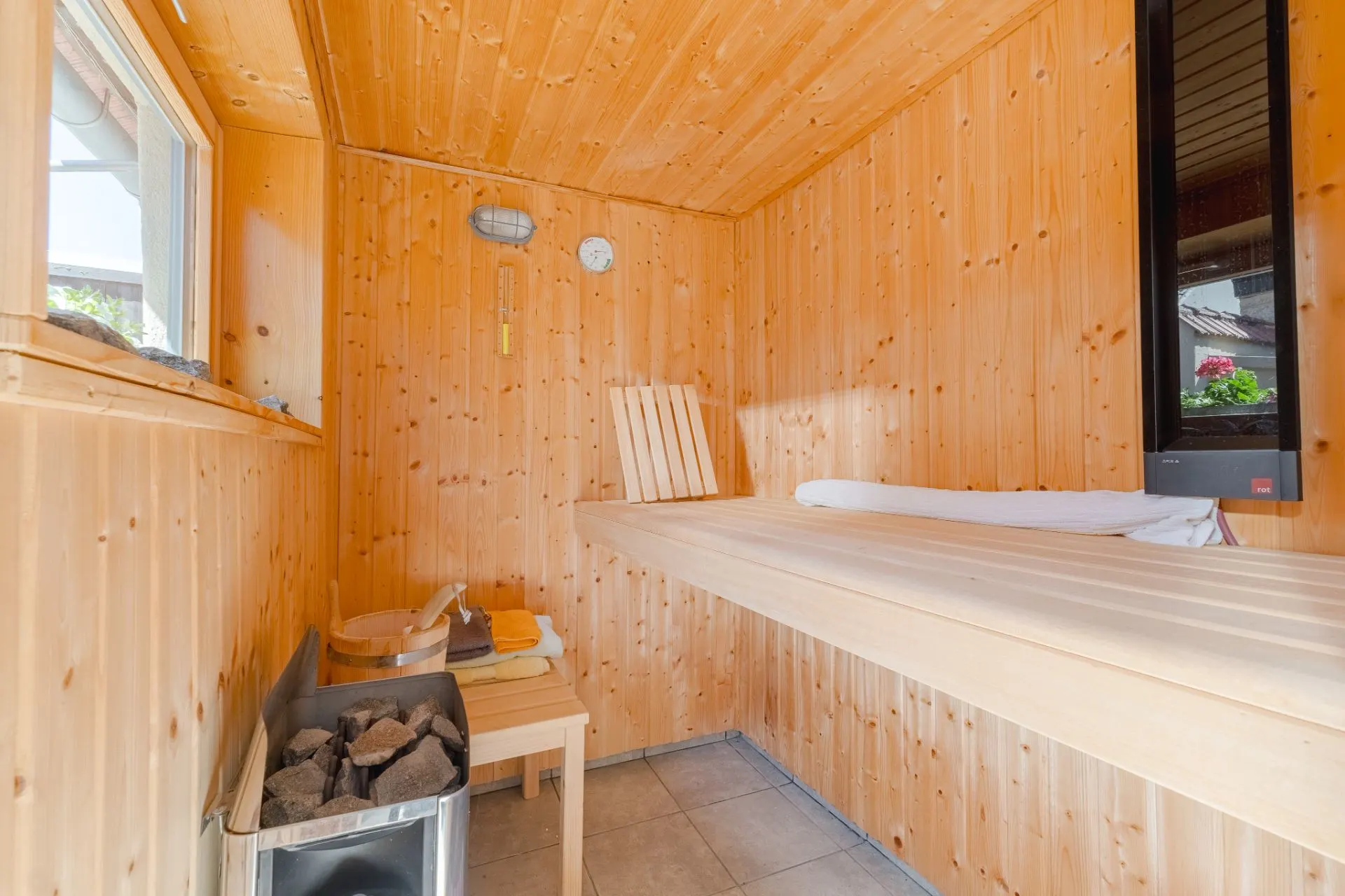 Holzsauna mit Bank, Fenster, Ofen und Handtüchern auf einem kleinen Tisch.