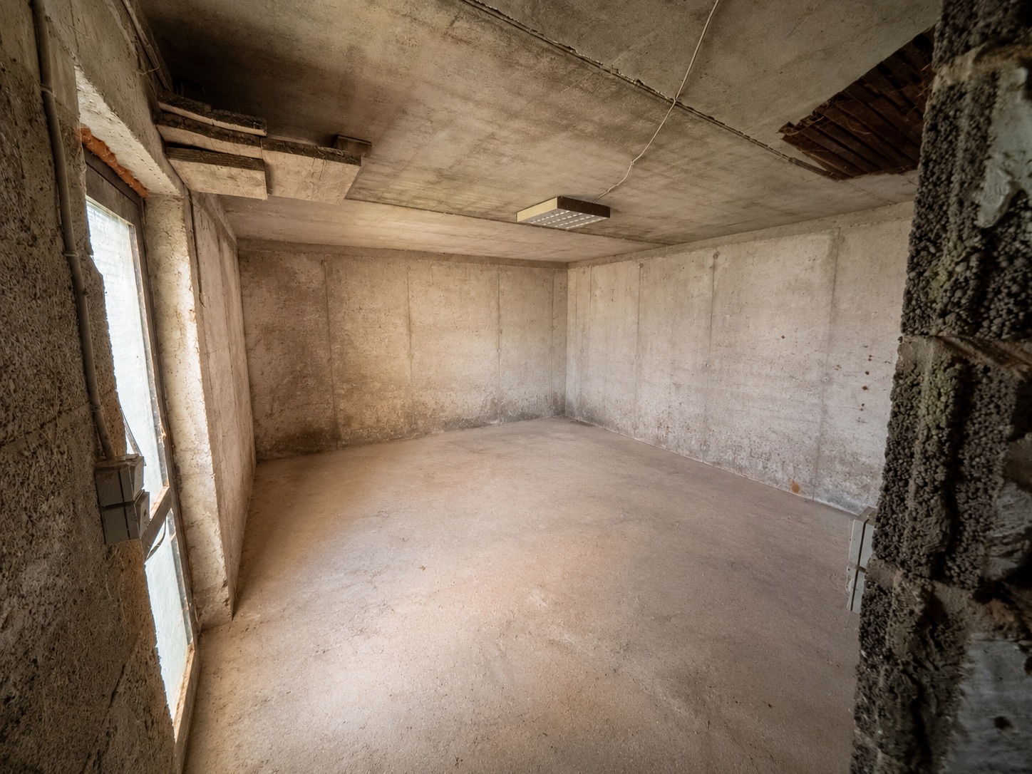 Leerer Kellerraum mit Betonwänden, Betonboden und Fenster auf der linken Seite.