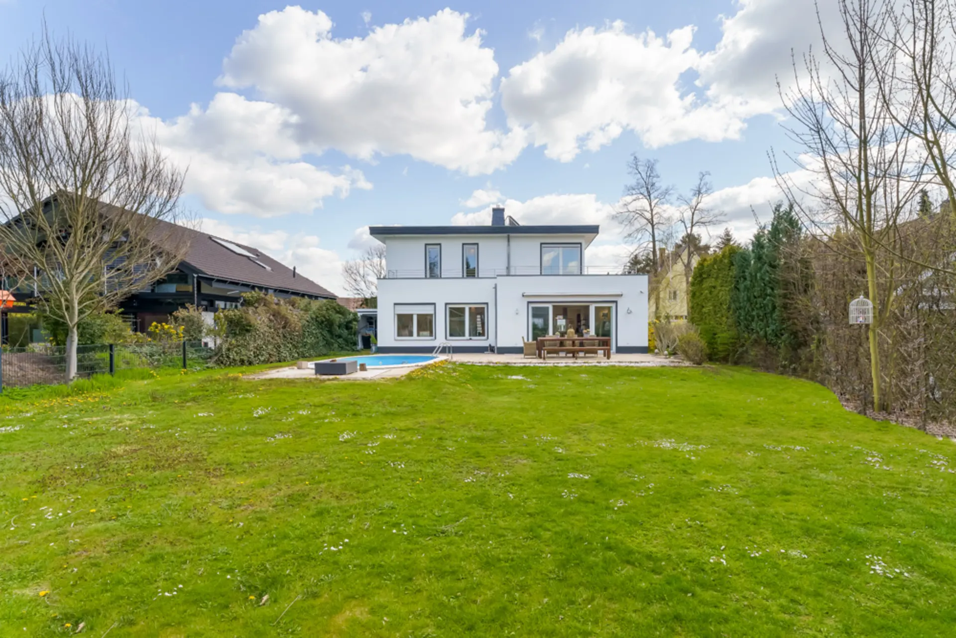 Modernes, weißes Wohnhaus mit großem Garten, Terrasse und Pool im Vordergrund.