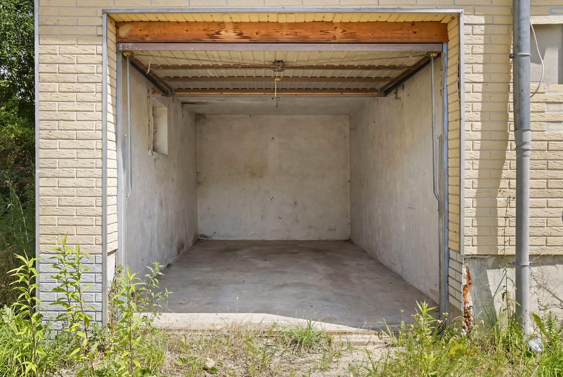 Leere Einzelgarage mit offenem Tor, Betonboden und einfachen Wänden.