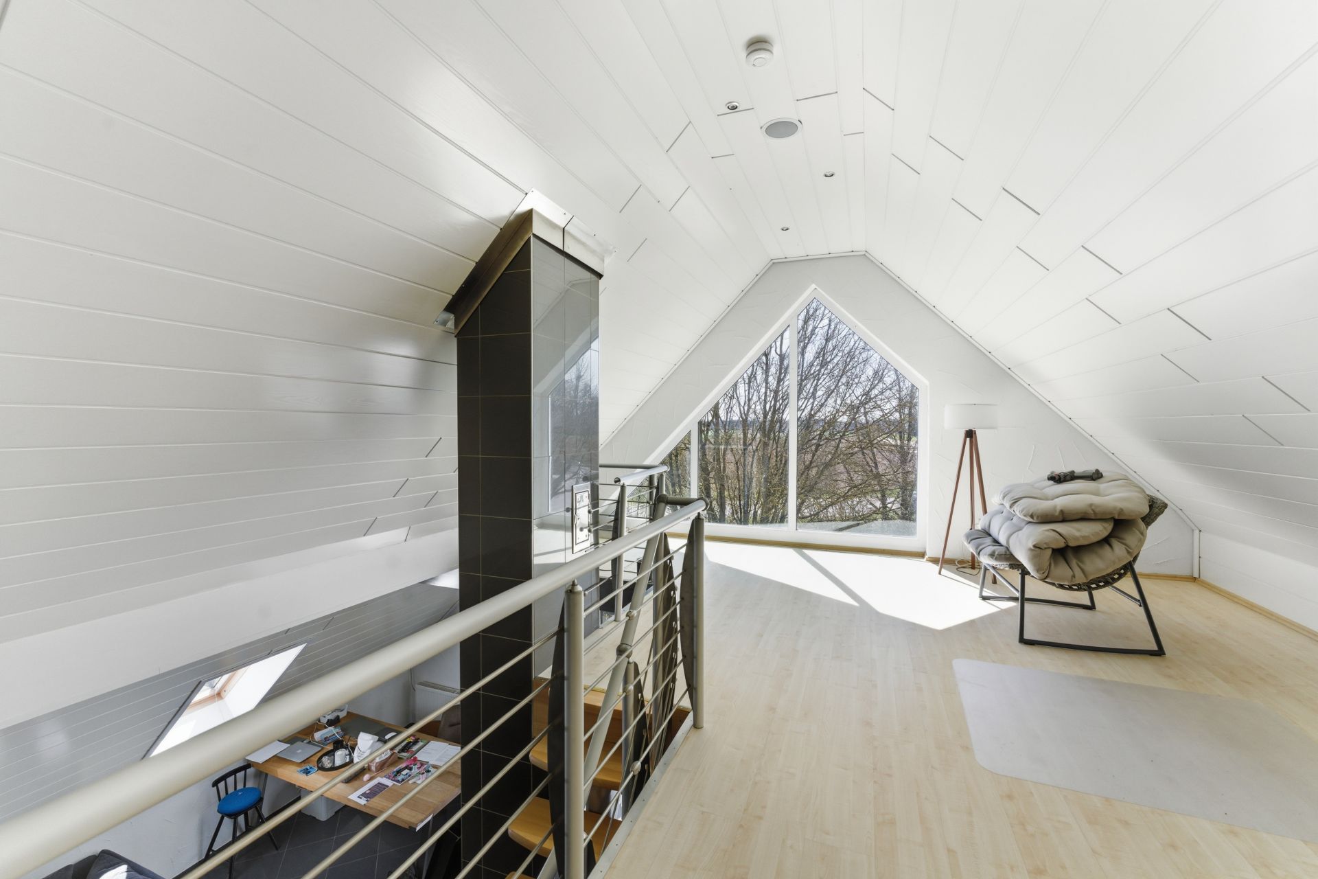Heller Dachbodenraum mit Schaukelstuhl, Schreibtisch und großem dreieckigem Fenster.
