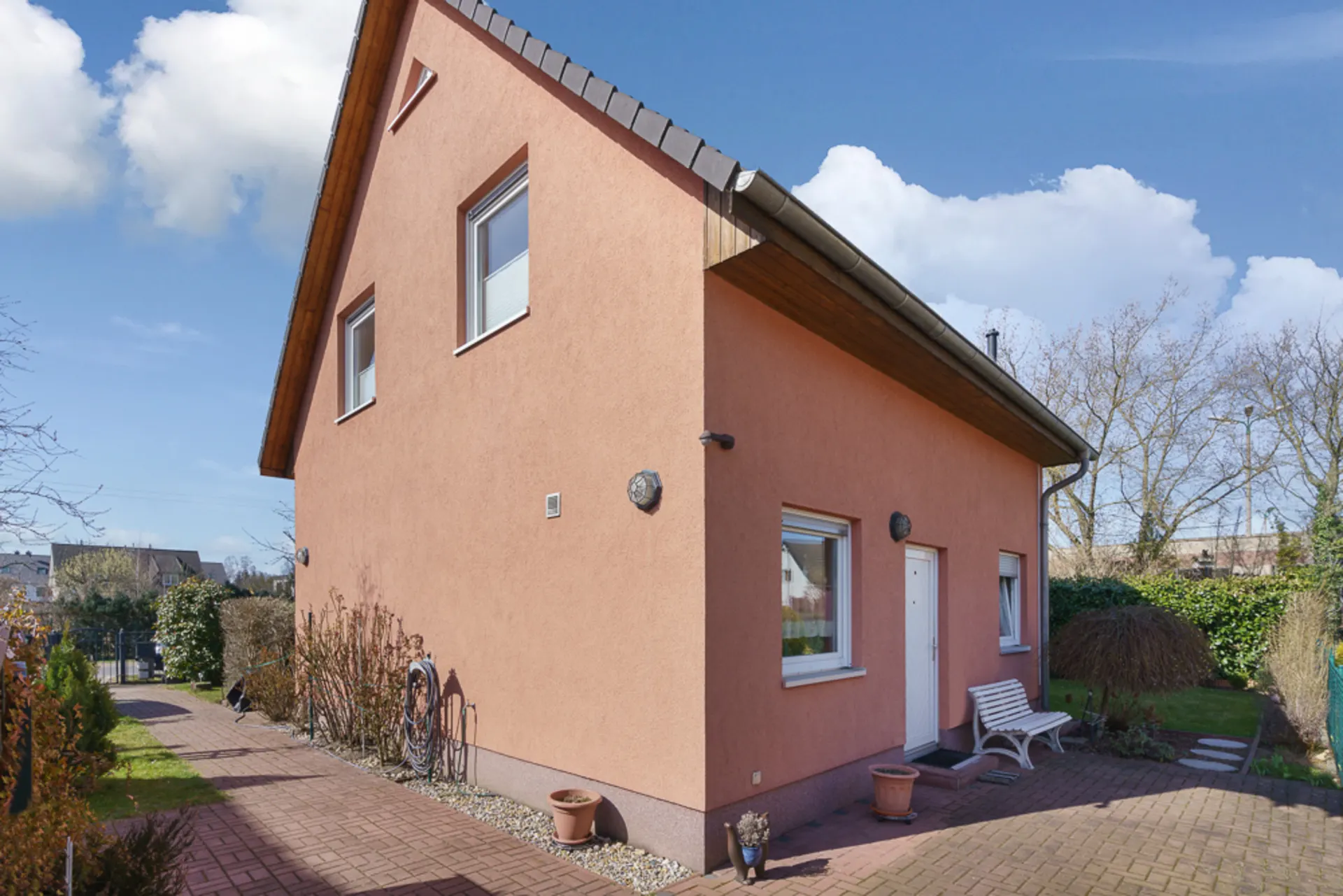 Einfamilienhaus mit rosafarbener Fassade, weißen Fenstern und kleinem Vorgarten bei Tageslicht.