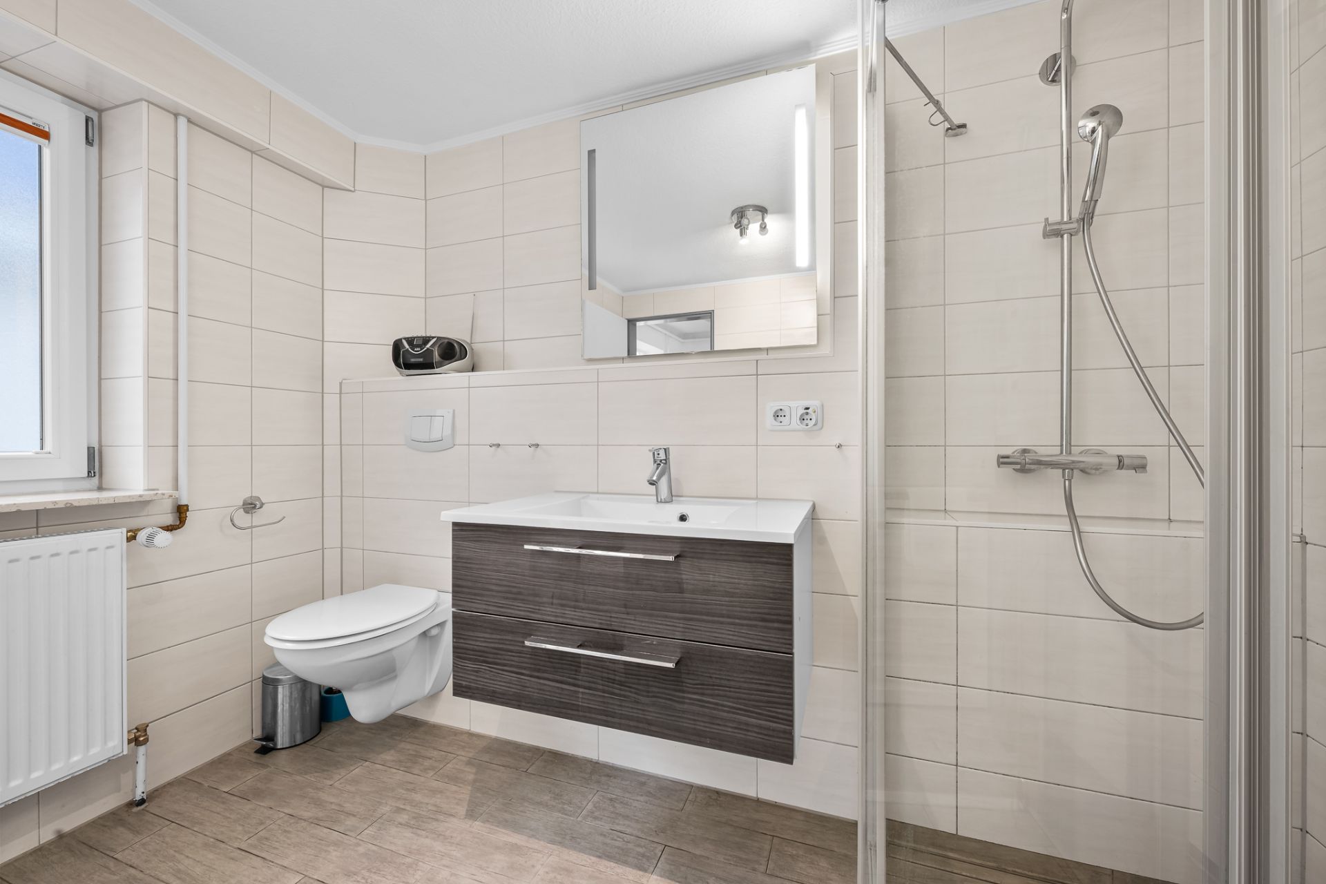 Helles Badezimmer mit Toilette, Waschbecken, Spiegel und offener Dusche.