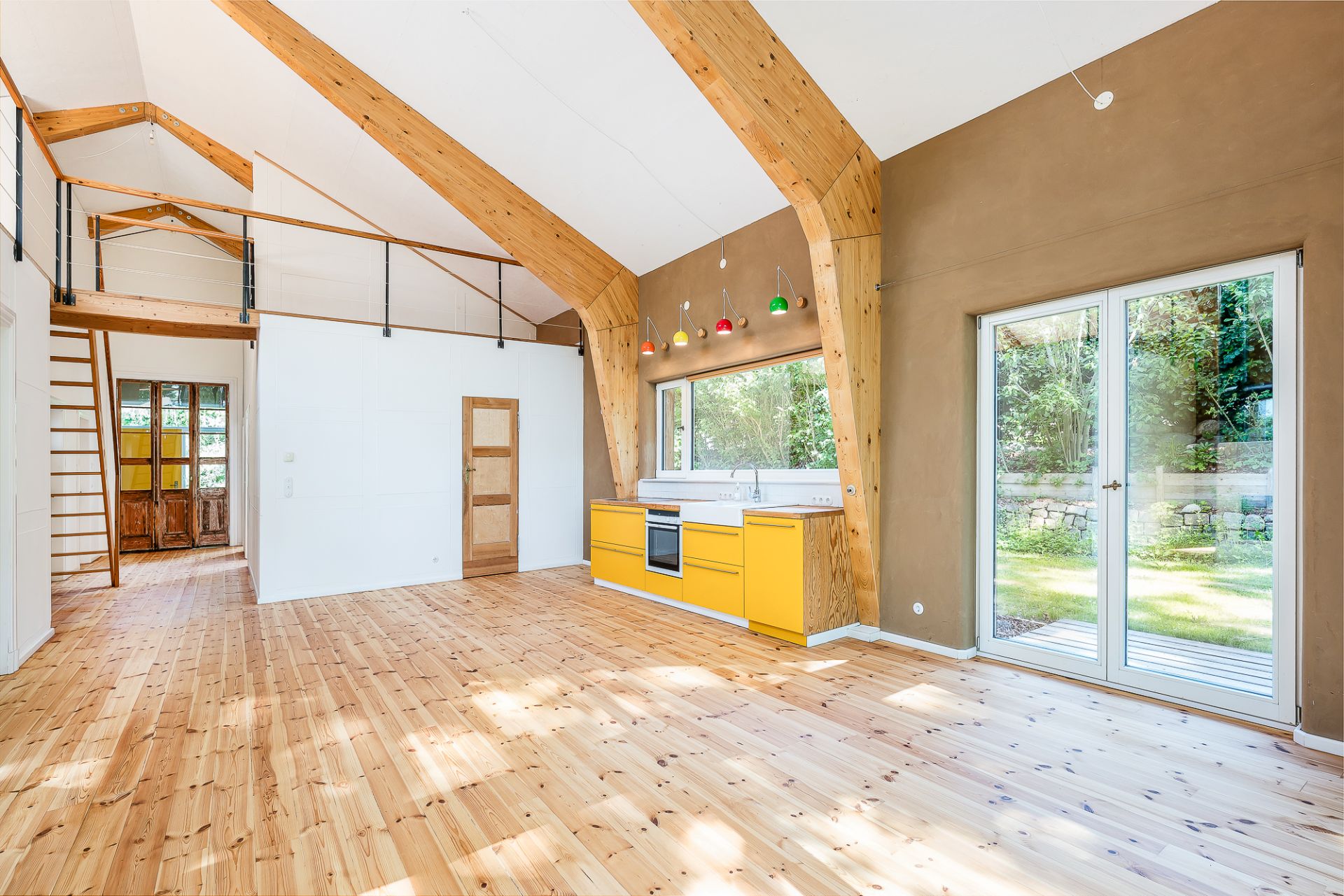 Heller Wohnraum mit Holzboden, offener Küche, großen Fenstern und Galerie mit Treppe.
