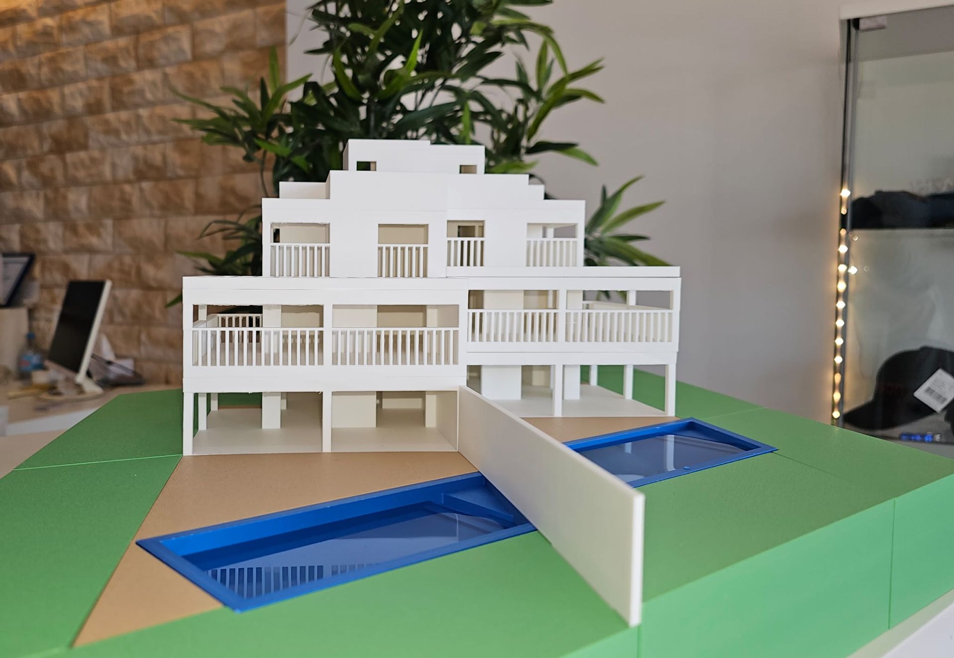 Architekturmodell eines weißen Wohngebäudes mit Pool und Balkon auf einem Tisch.