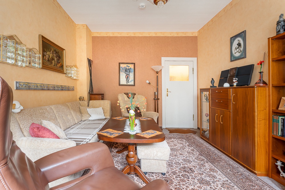 Gemütliches Wohnzimmer mit Sofa, Teppich, Couchtisch und Holzschrank, dekoriert mit Bildern und Blumen.