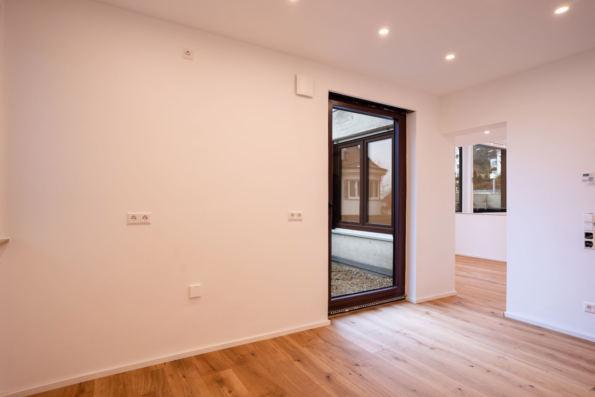 Heller Raum mit Holzfußboden, weißer Wand und großem Fenster zur Terrasse.
