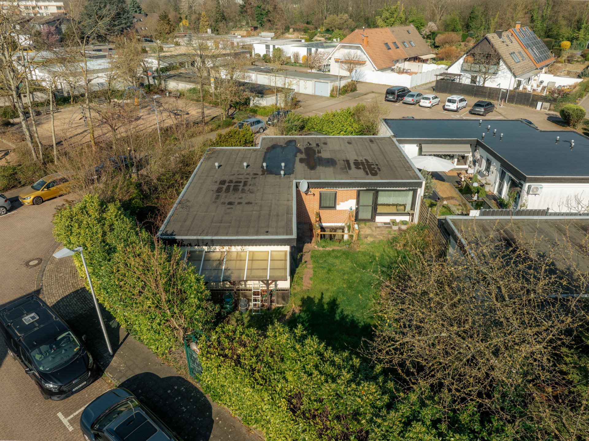 Luftaufnahme eines einstöckigen Wohnhauses mit Flachdach, Garten und nahegelegenen geparkten Autos.