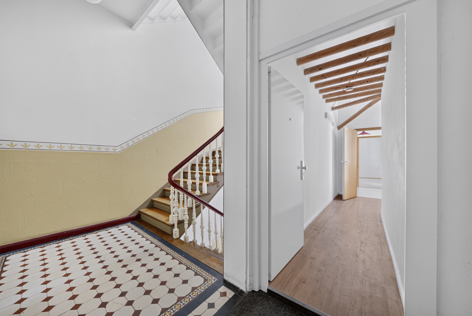 Treppenhaus mit gemustertem Fliesenboden und Flur mit sichtbaren Holzbalken.