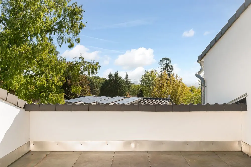 Blick von einer Terrasse mit Fliesenboden auf Bäume und einen bewölkten Himmel.