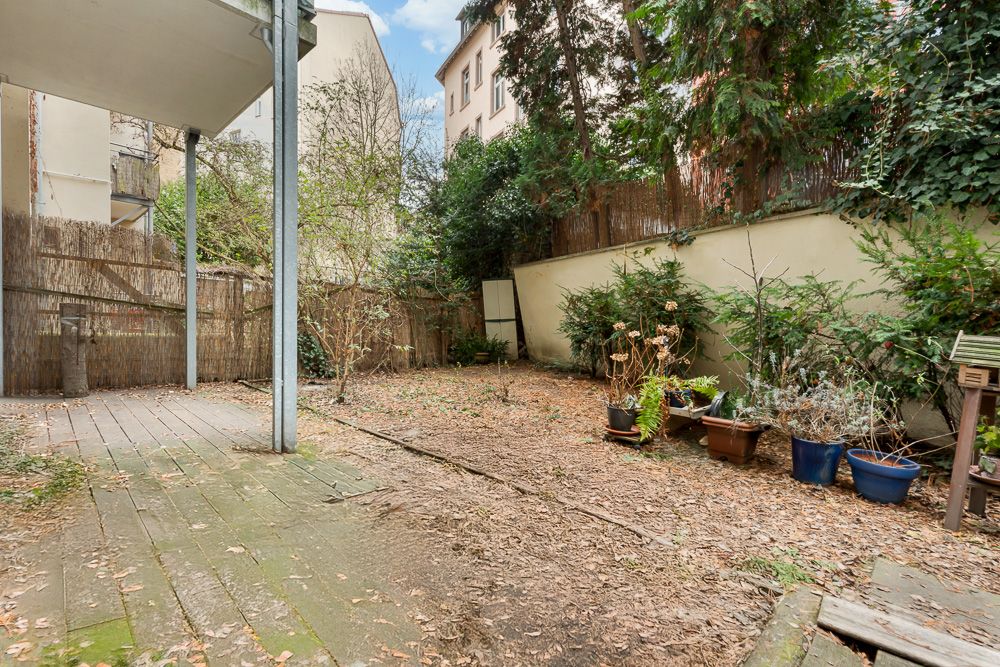 Hinterhof mit Terrasse, Topfpflanzen und Bäumen, umgeben von Mauern und Holzzaun.