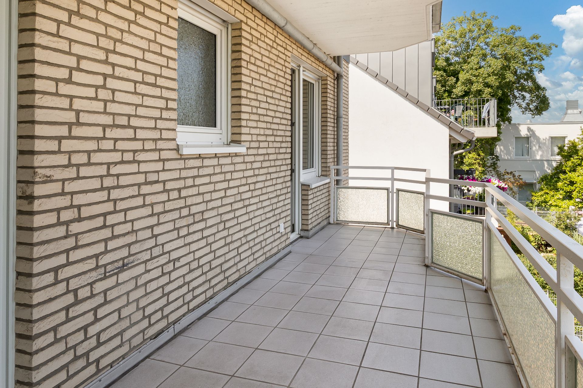 Geräumiger Balkon mit Fliesenboden und Geländer, angrenzend an eine Hauswand mit Fenstern.