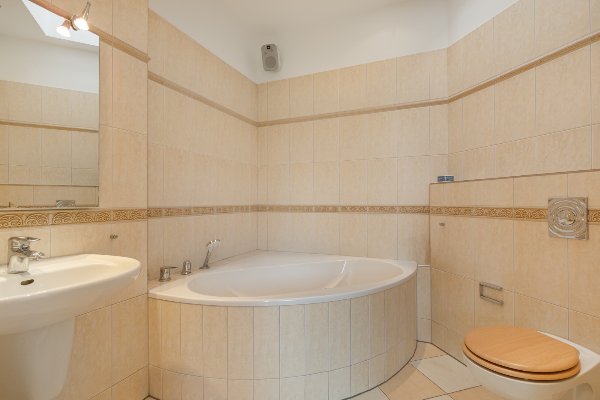 Helles Badezimmer mit Eckbadewanne, Waschbecken und Toilette mit Holzbretdeckel.