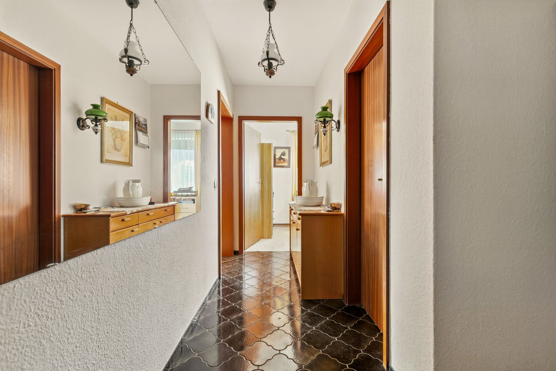 Heller Flur mit Spiegel, Kommoden, dunklem Boden und Holztüren in einer Wohnung.