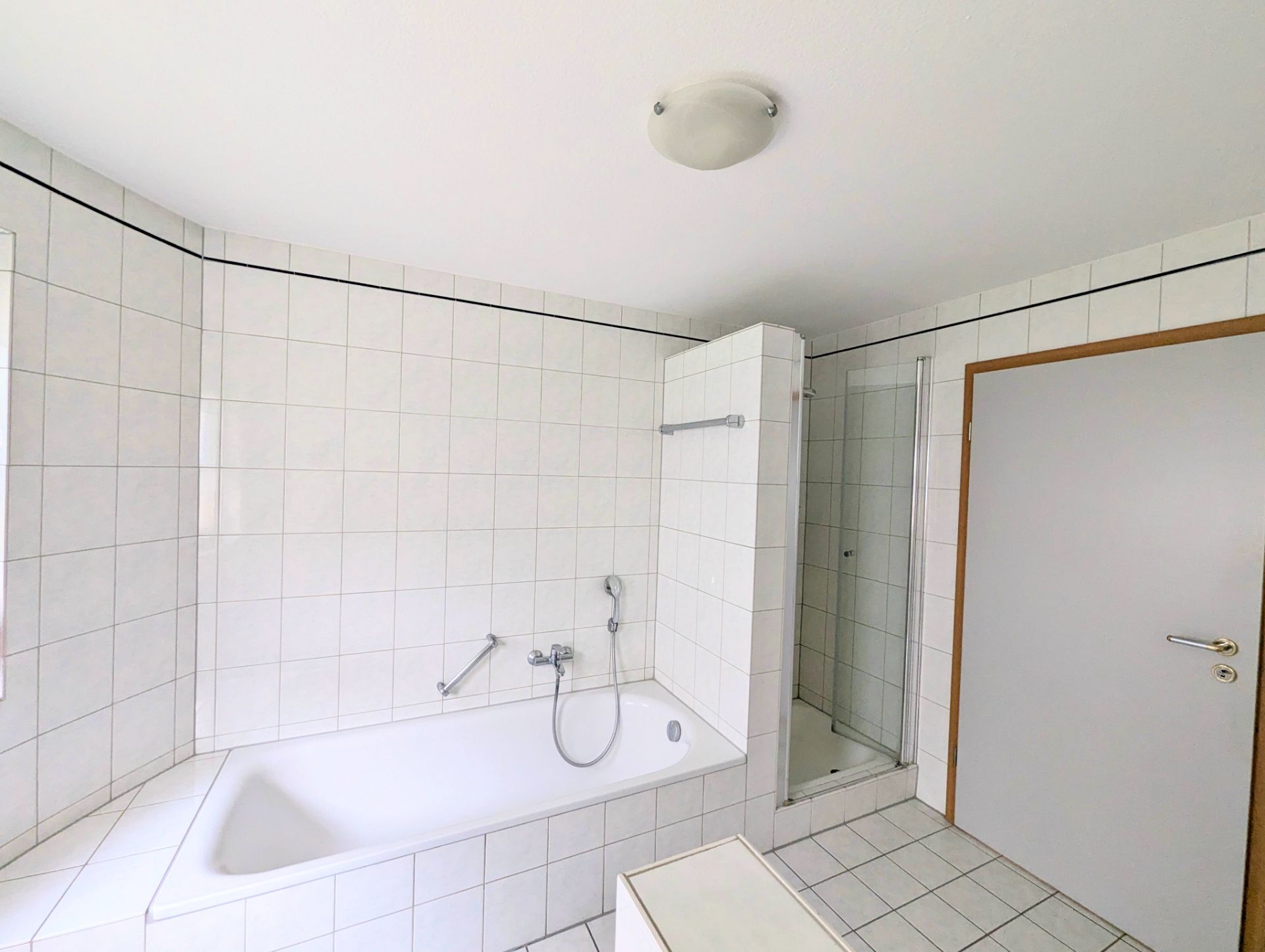 Helles Badezimmer mit Badewanne, Dusche und weiß gefliesten Wänden.