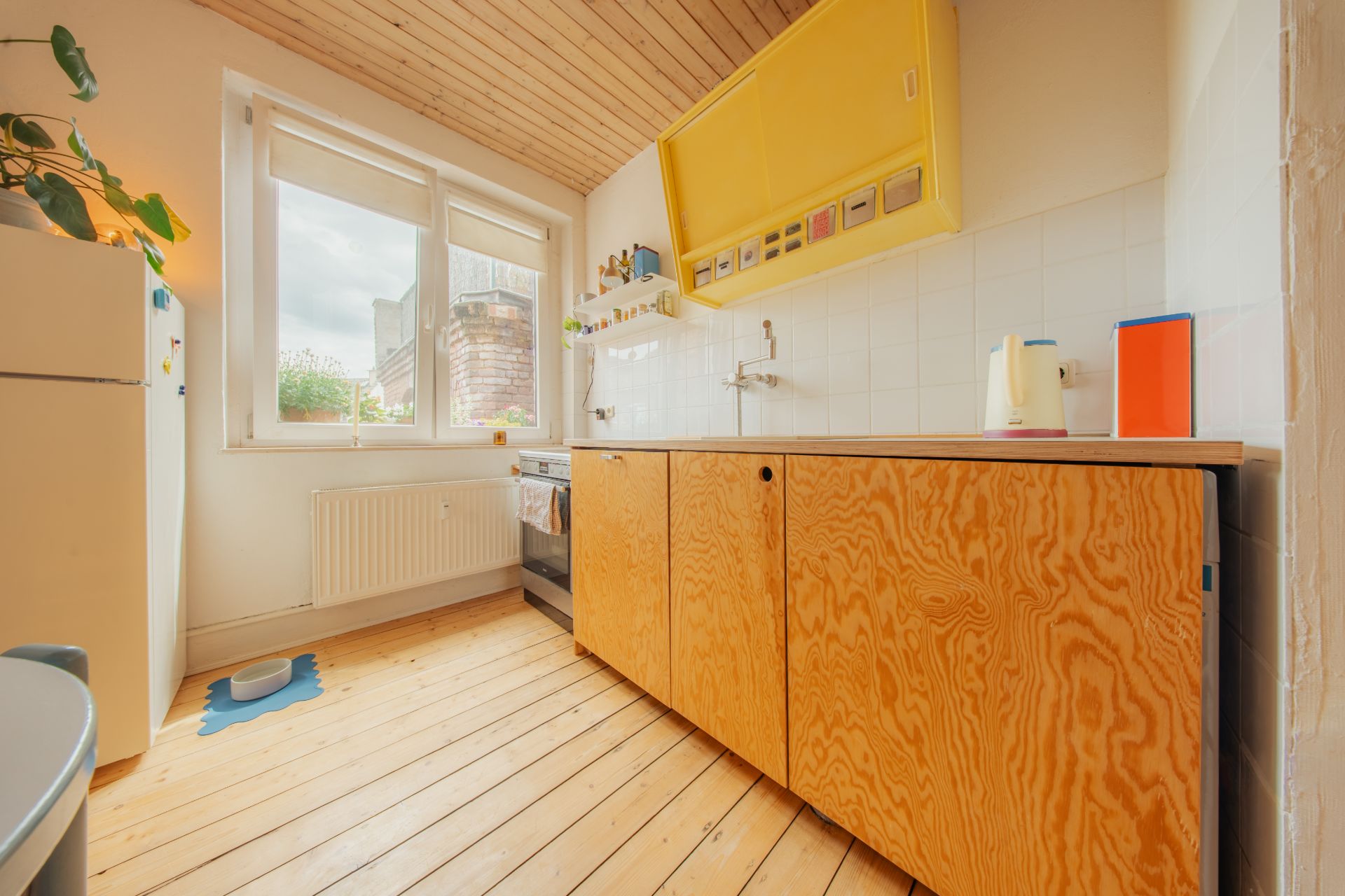 Helle Küche mit Holzboden, gelbem Oberschrank und großem Fenster.