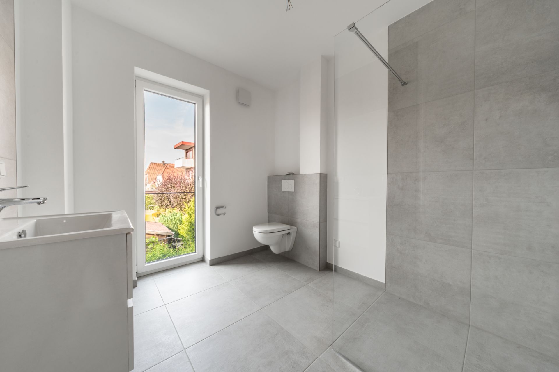 Modernes Badezimmer mit bodengleicher Dusche, WC, Waschbecken und großem Fenster mit Blick nach draußen.