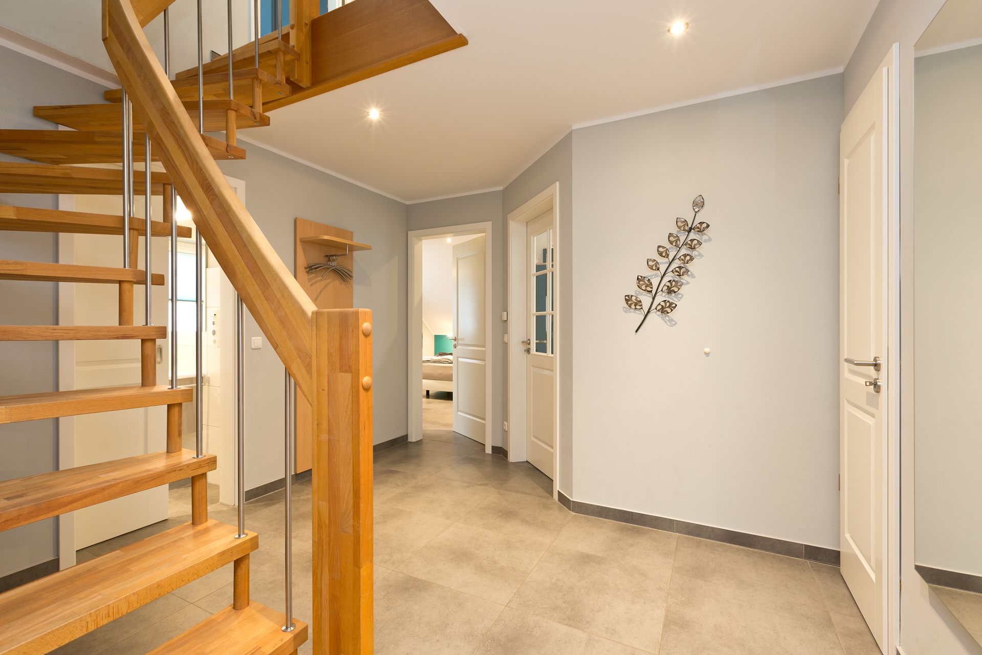 Heller Flur mit Holztreppe, grauem Boden und dekorativem Wandbild in Blattform.