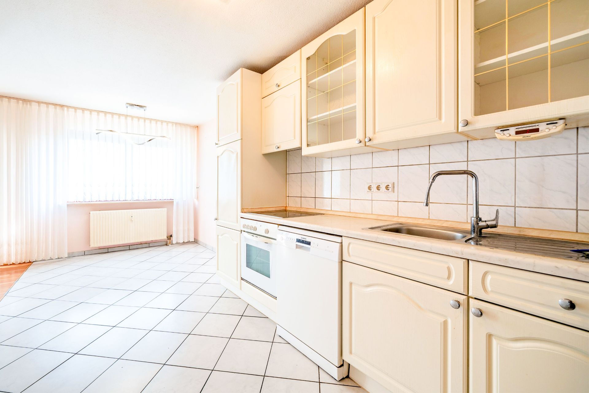 Helle Einbauküche mit weißen Schränken, Backofen, Spülmaschine und Fliesenspiegel.
