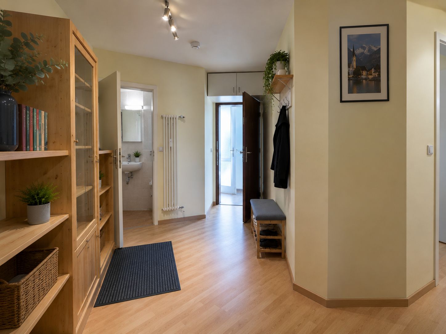 Heller Flur mit Holzboden, Regal, Garderobe, Sitzbank und Zugang zu Bad und Tür.