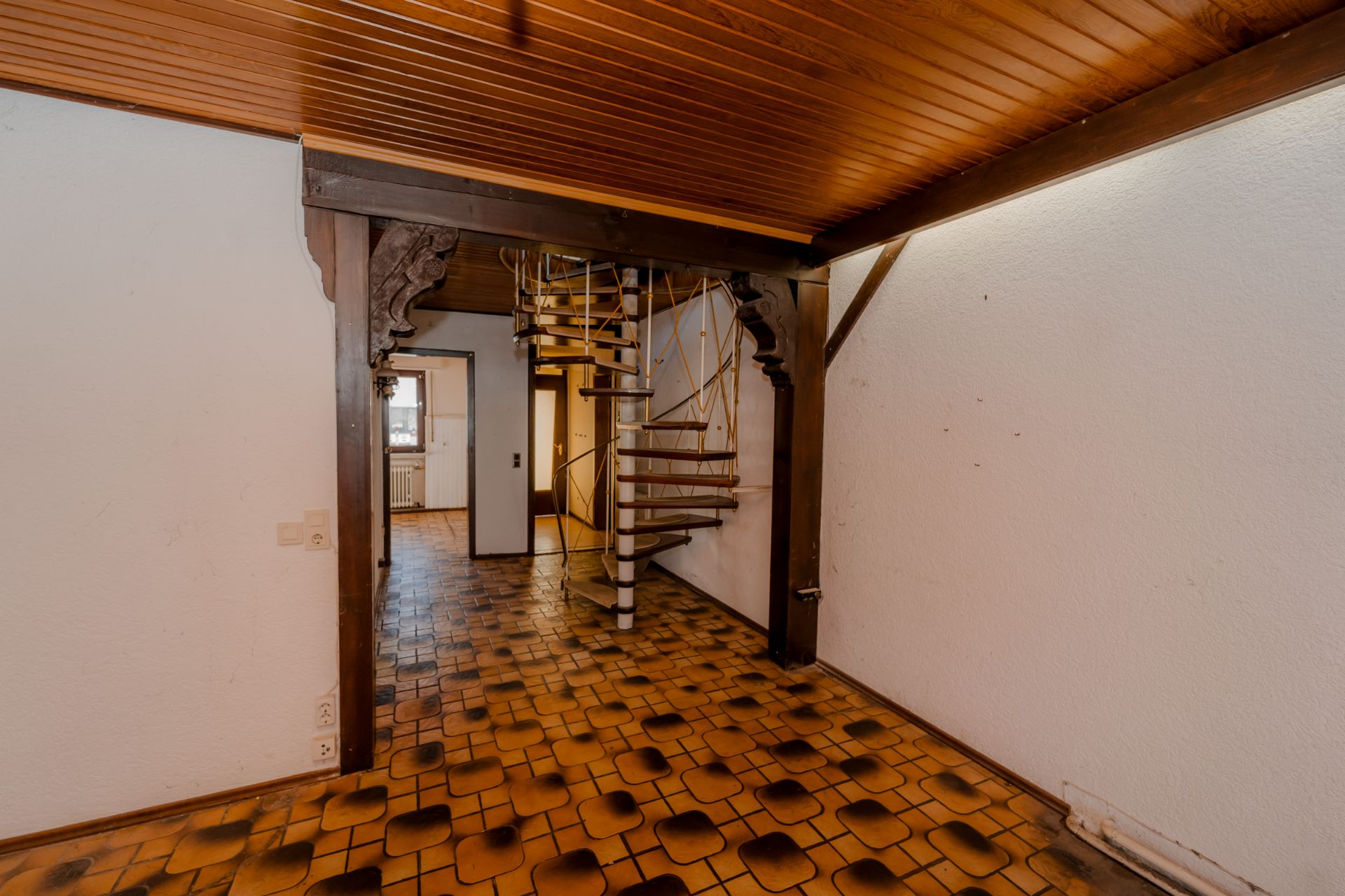 Raum mit braunem Fliesenboden, Holzdecke und einer Wendeltreppe aus Metall.