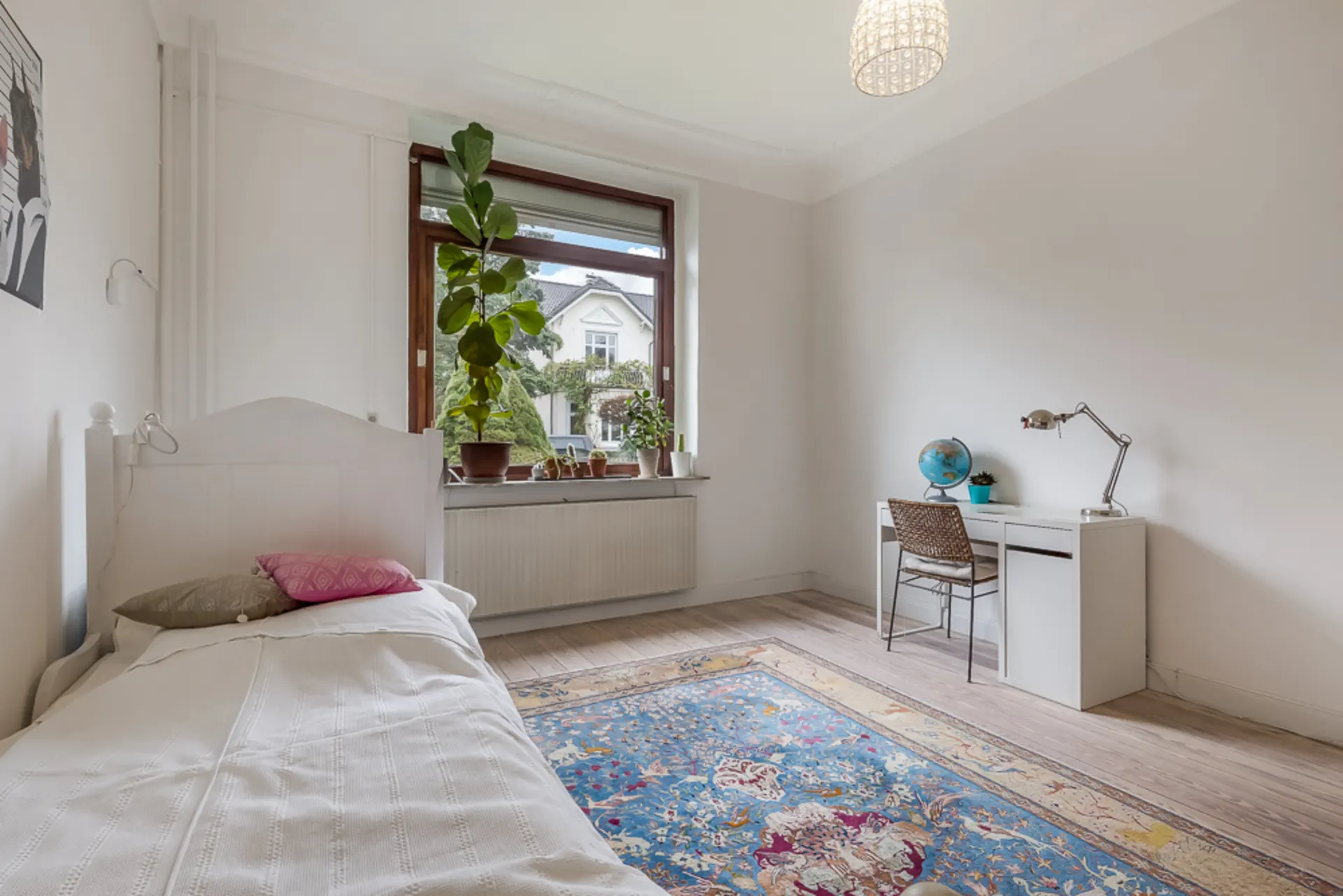 Helles Schlafzimmer mit Einzelbett, Schreibtisch, Stuhl, Fenster und Pflanzen auf der Fensterbank.